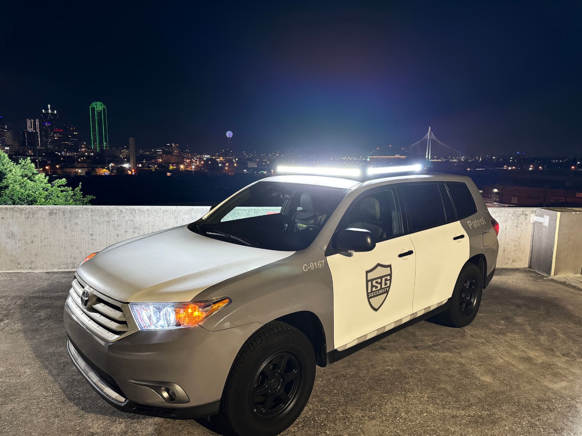 ISG Security patrol truck with its white light bar on, on a rooftop with the Dallas skyline at night behind it